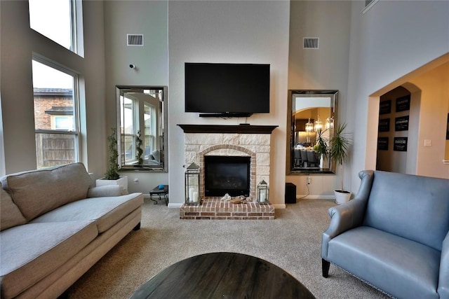 carpeted living room with a stone fireplace, a high ceiling, and an inviting chandelier