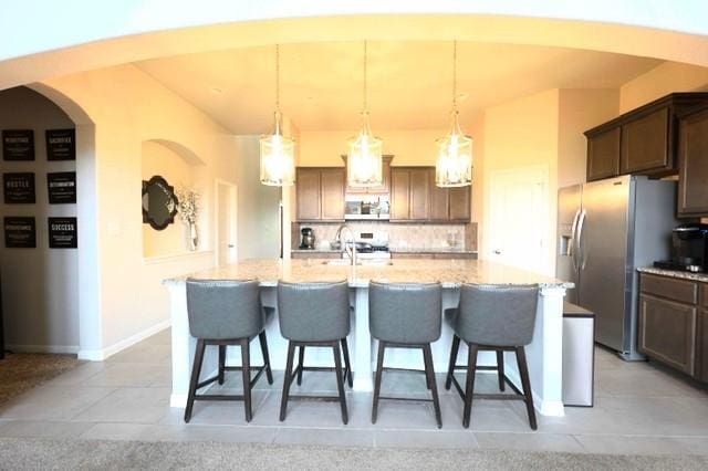 kitchen with decorative light fixtures, a kitchen island with sink, appliances with stainless steel finishes, and tasteful backsplash