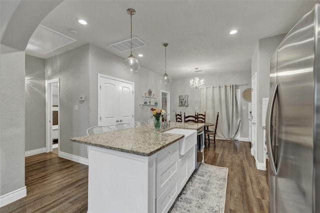 kitchen featuring stainless steel refrigerator, white cabinetry, dark hardwood / wood-style flooring, pendant lighting, and a kitchen island with sink