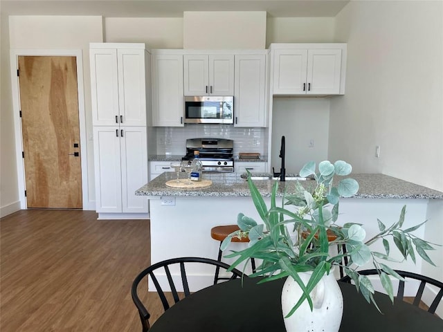 kitchen with light stone counters, backsplash, white cabinetry, and appliances with stainless steel finishes