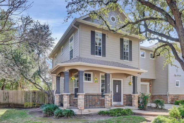 american foursquare style home featuring a garage, covered porch, stone siding, and fence