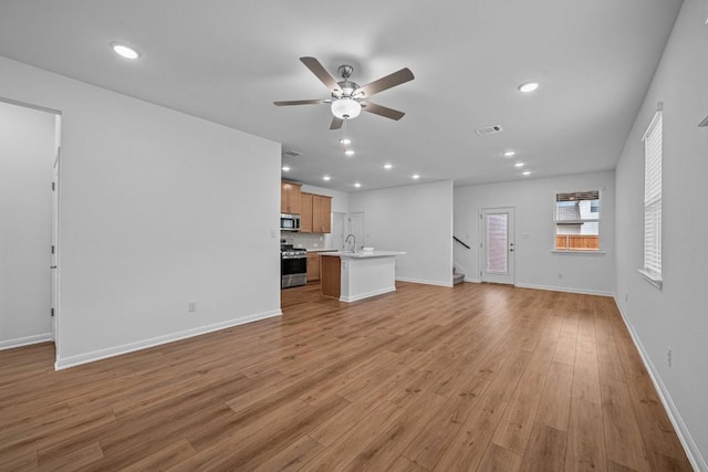 unfurnished living room with ceiling fan, sink, and light hardwood / wood-style flooring