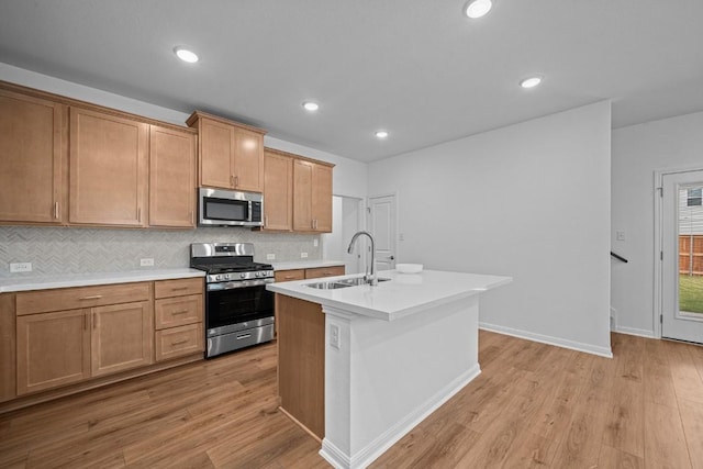 kitchen featuring decorative backsplash, stainless steel appliances, a kitchen island with sink, sink, and light hardwood / wood-style flooring