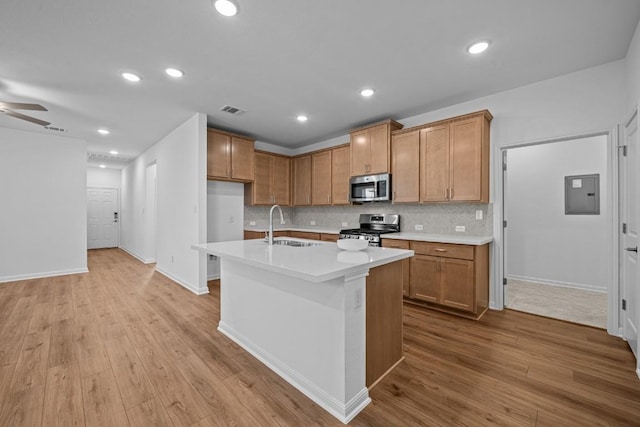 kitchen with light hardwood / wood-style floors, stainless steel appliances, a kitchen island with sink, sink, and electric panel