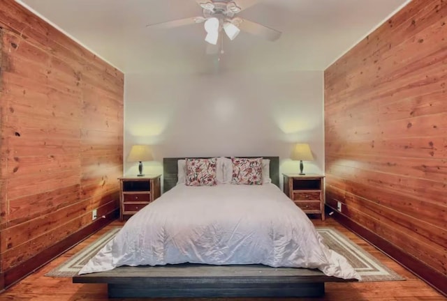 bedroom featuring hardwood / wood-style flooring, ceiling fan, and wooden walls