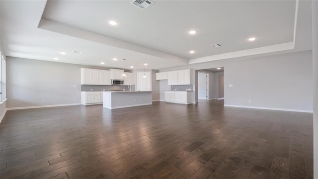 unfurnished living room featuring a raised ceiling and dark hardwood / wood-style flooring