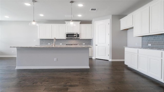 kitchen with white cabinetry, light stone countertops, an island with sink, and decorative light fixtures