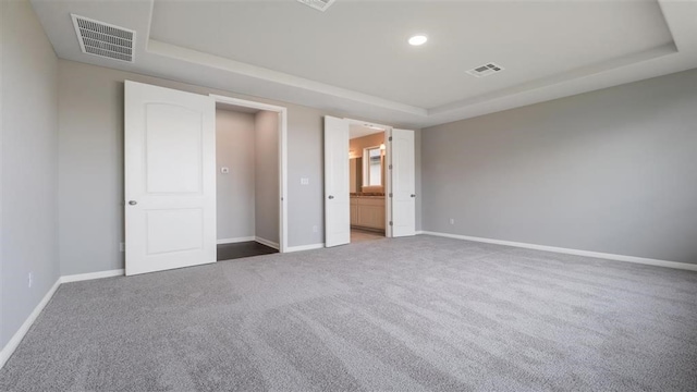 unfurnished bedroom featuring carpet flooring, ensuite bathroom, and a raised ceiling