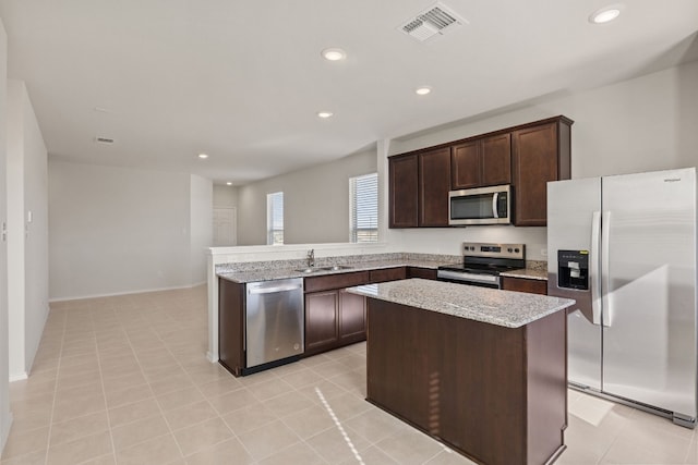 kitchen with dark brown cabinetry, sink, light stone counters, a kitchen island, and appliances with stainless steel finishes