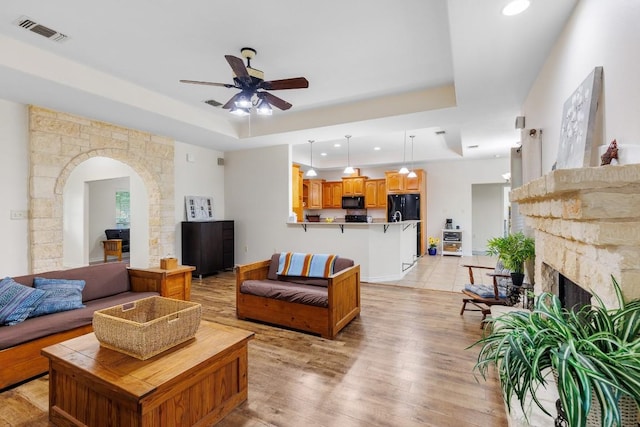 living room featuring a fireplace, light wood-type flooring, a raised ceiling, and ceiling fan