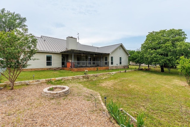 rear view of property featuring a fire pit and a lawn