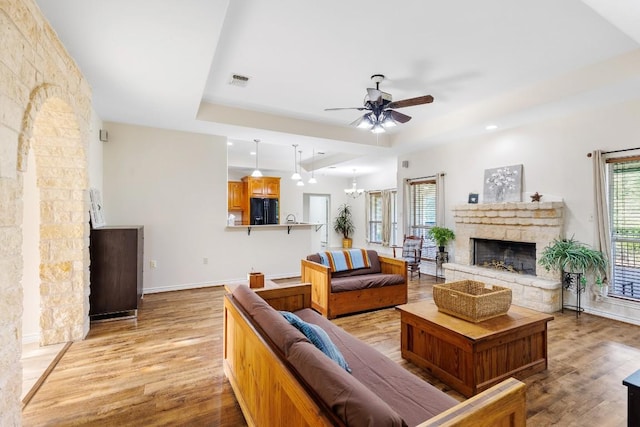 living room featuring ceiling fan with notable chandelier, a stone fireplace, and light hardwood / wood-style flooring