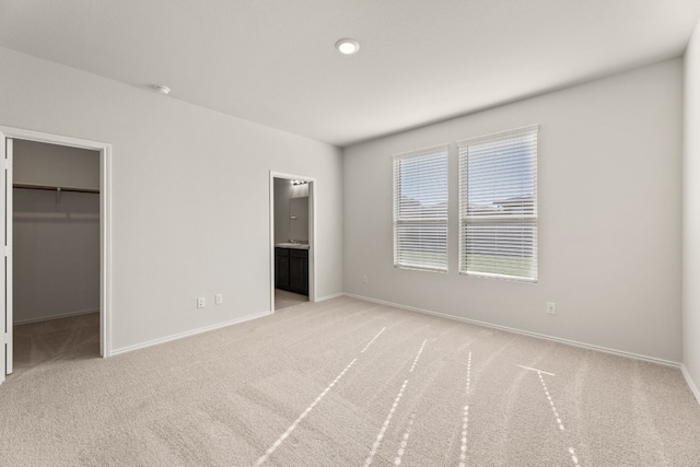 unfurnished bedroom with a closet, light colored carpet, a walk in closet, and ensuite bath