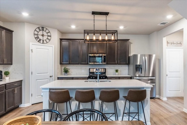 kitchen with a kitchen island with sink, dark brown cabinets, stainless steel appliances, and light hardwood / wood-style floors