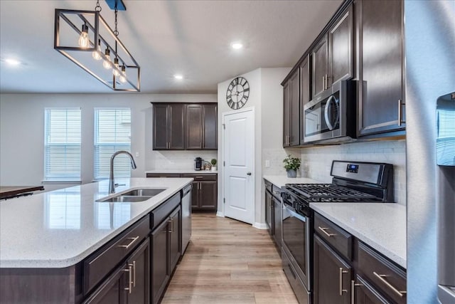 kitchen featuring stainless steel appliances, sink, decorative light fixtures, light hardwood / wood-style flooring, and an island with sink