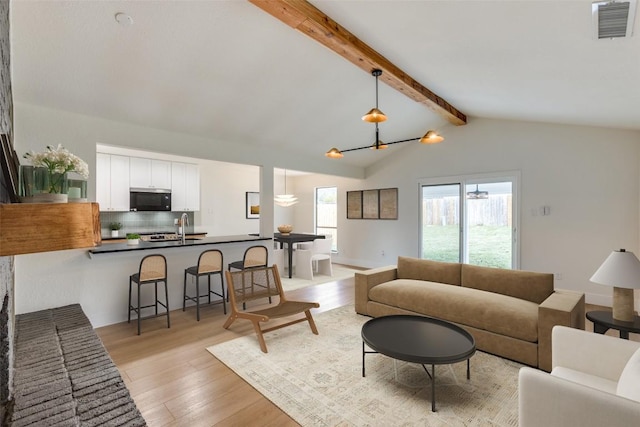 living room with vaulted ceiling with beams, sink, and light hardwood / wood-style floors