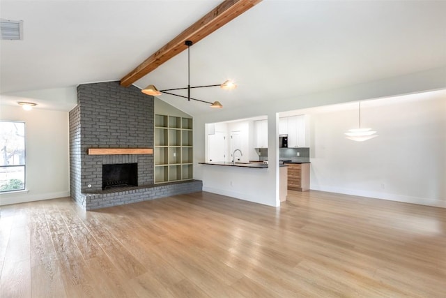 unfurnished living room featuring sink, a brick fireplace, vaulted ceiling with beams, a notable chandelier, and light hardwood / wood-style floors