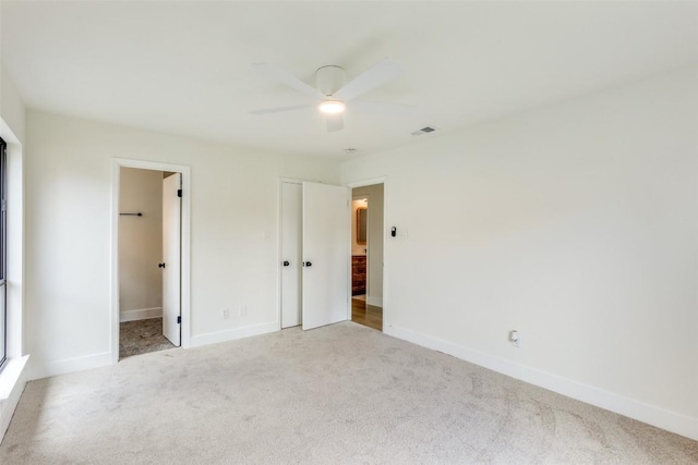 unfurnished bedroom featuring ceiling fan, a spacious closet, light carpet, and a closet