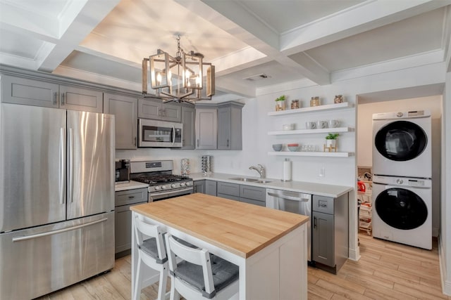 kitchen featuring a center island, coffered ceiling, stacked washer / drying machine, beam ceiling, and stainless steel appliances