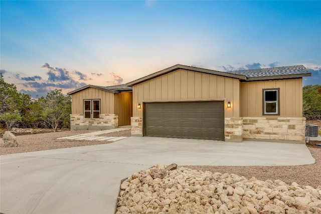 view of front of home with a garage, board and batten siding, concrete driveway, stone siding, and central AC