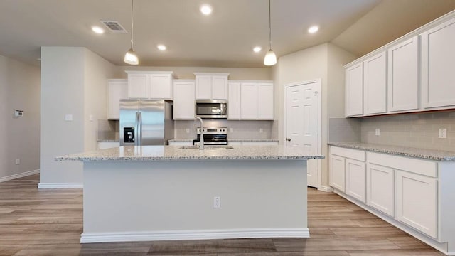 kitchen with pendant lighting, white cabinets, stainless steel appliances, and light hardwood / wood-style floors