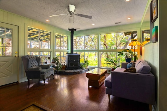 sunroom / solarium with ceiling fan, a wood stove, and a wealth of natural light