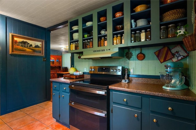 kitchen with stainless steel range with electric stovetop, wood walls, light tile patterned floors, and blue cabinetry