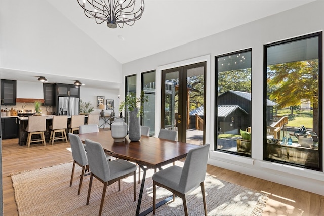 dining space with a notable chandelier, light hardwood / wood-style floors, high vaulted ceiling, and french doors