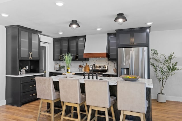 kitchen featuring stainless steel appliances, an AC wall unit, a kitchen island with sink, custom exhaust hood, and light wood-type flooring