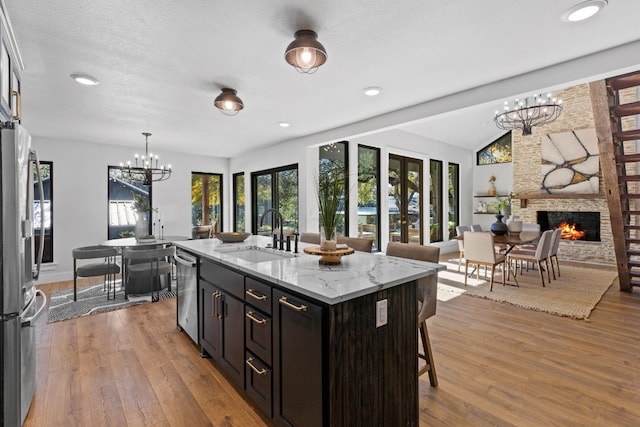 kitchen with french doors, light stone counters, sink, a center island with sink, and a fireplace