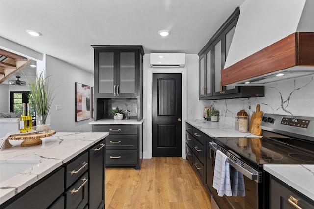 kitchen with backsplash, premium range hood, electric range, a wall mounted AC, and light hardwood / wood-style floors