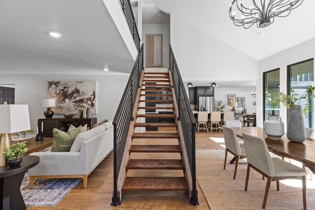 staircase with high vaulted ceiling, wood-type flooring, and a notable chandelier