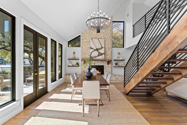 dining space featuring french doors, high vaulted ceiling, a notable chandelier, wood-type flooring, and a fireplace