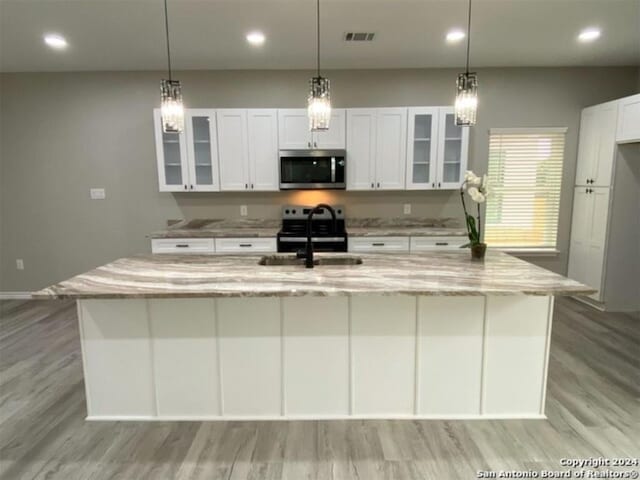 kitchen featuring white cabinets, sink, light stone countertops, an island with sink, and light hardwood / wood-style floors