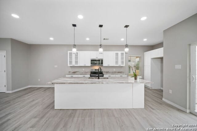 kitchen with white cabinets, light stone countertops, stainless steel appliances, and a kitchen island with sink