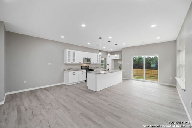 kitchen featuring light wood-type flooring, stainless steel appliances, pendant lighting, white cabinets, and an island with sink