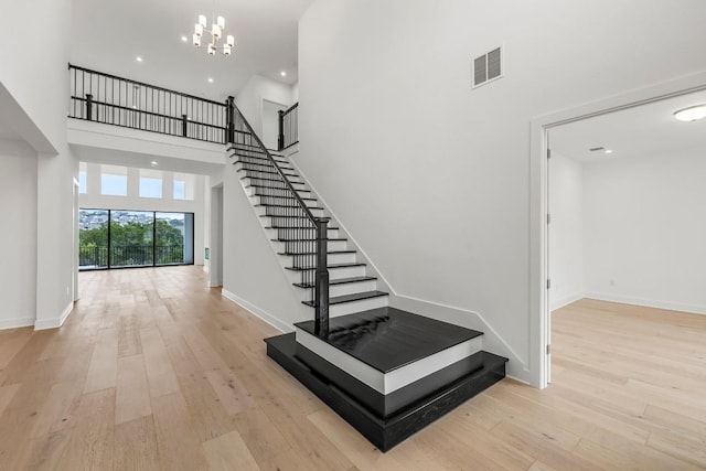 stairs featuring hardwood / wood-style floors, a towering ceiling, and a chandelier