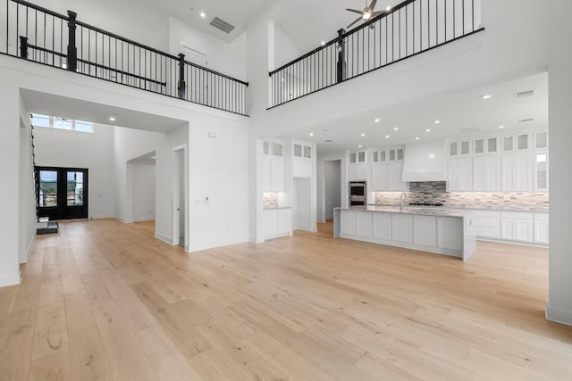 unfurnished living room with ceiling fan, a towering ceiling, light wood-type flooring, and french doors