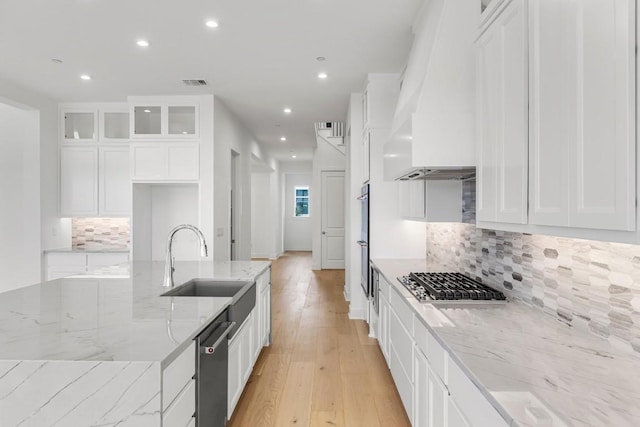 kitchen with sink, custom exhaust hood, stainless steel appliances, light stone countertops, and white cabinets