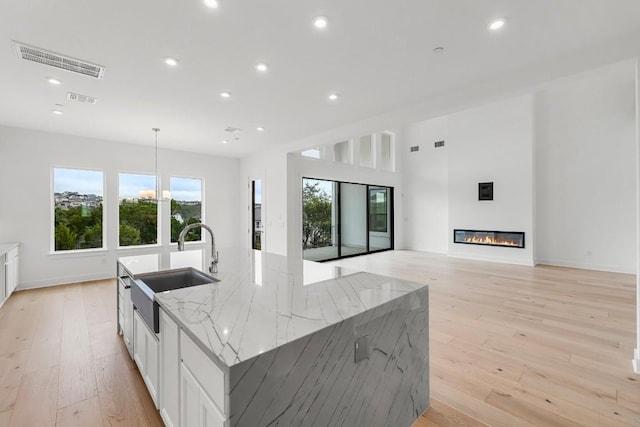 kitchen featuring white cabinets, light stone countertops, sink, and a large island with sink