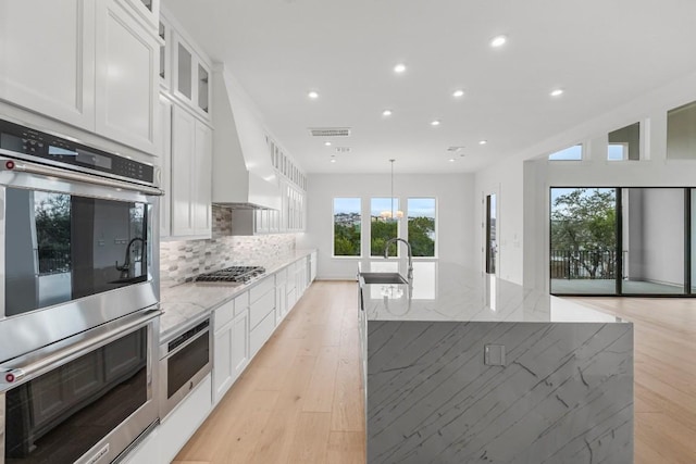 kitchen featuring light stone countertops, a center island with sink, and white cabinets