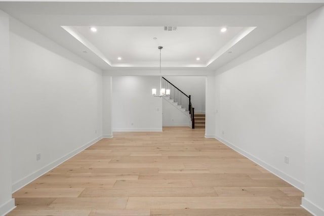 unfurnished living room with light hardwood / wood-style flooring, a chandelier, and a tray ceiling