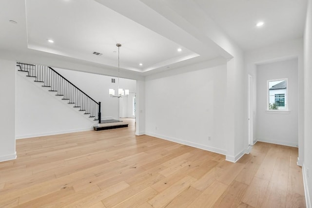 unfurnished living room with light hardwood / wood-style floors, a raised ceiling, and a chandelier