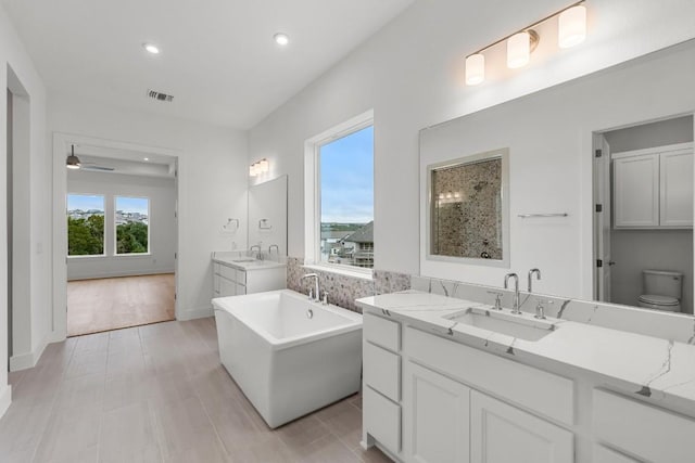 bathroom with ceiling fan, tile patterned flooring, a bathing tub, vanity, and toilet