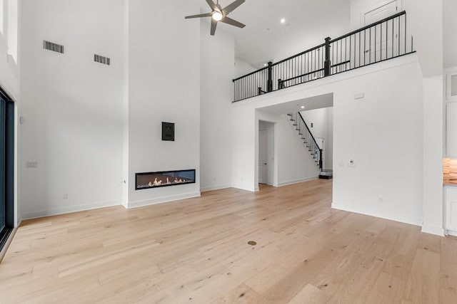 unfurnished living room featuring ceiling fan, light wood-type flooring, and a high ceiling