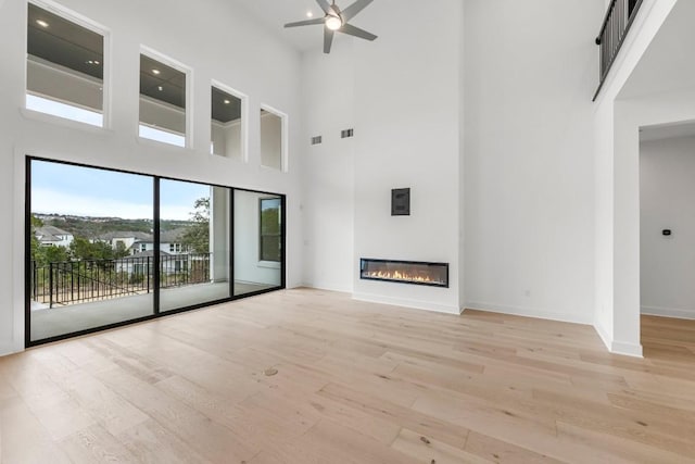 unfurnished living room with ceiling fan, light hardwood / wood-style floors, and a high ceiling