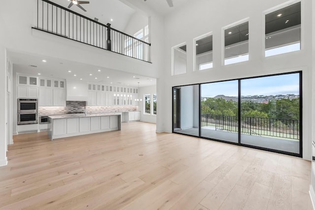 unfurnished living room with a towering ceiling, ceiling fan, and light hardwood / wood-style flooring