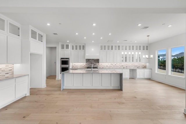 kitchen featuring sink, white cabinetry, tasteful backsplash, pendant lighting, and a kitchen island with sink