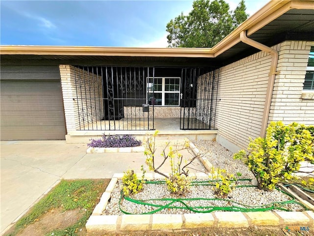 view of exterior entry featuring brick siding, a garage, and driveway