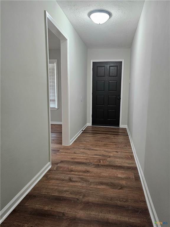 doorway featuring baseboards, a textured ceiling, and dark wood-style flooring